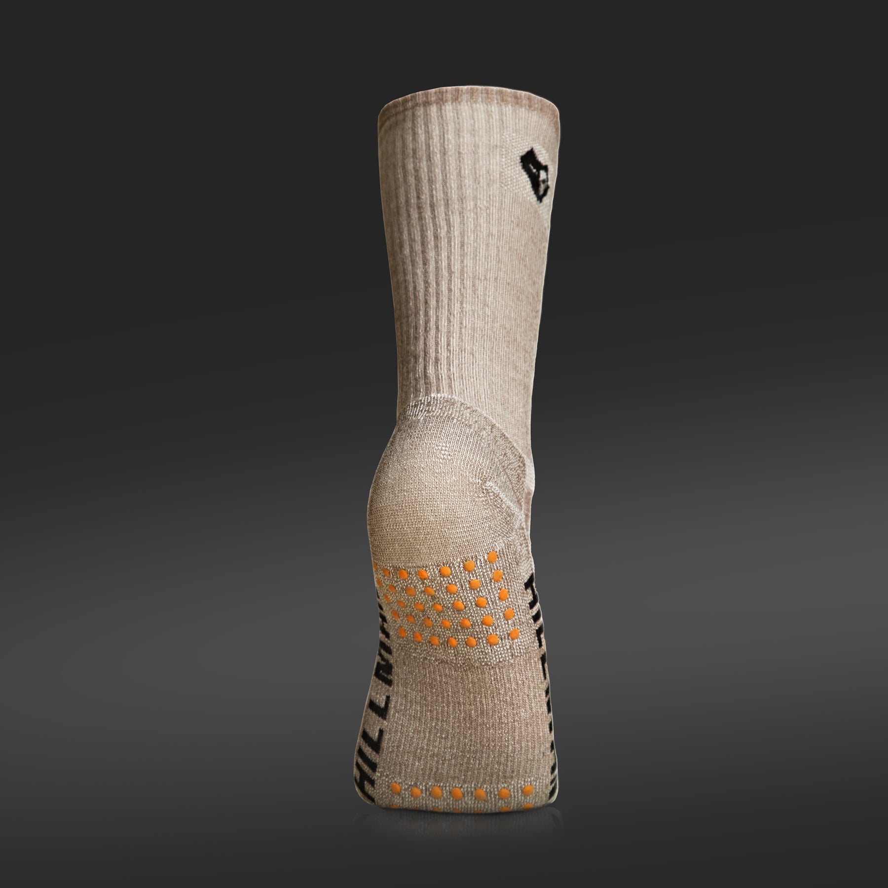 A Hillman® Hunting Socks Merino Wool in beige stands upright on a dark gradient, heel and orange grippy dots visible. Black side text is partly shown. Designed as the warmest socks for extreme cold weather adventures.