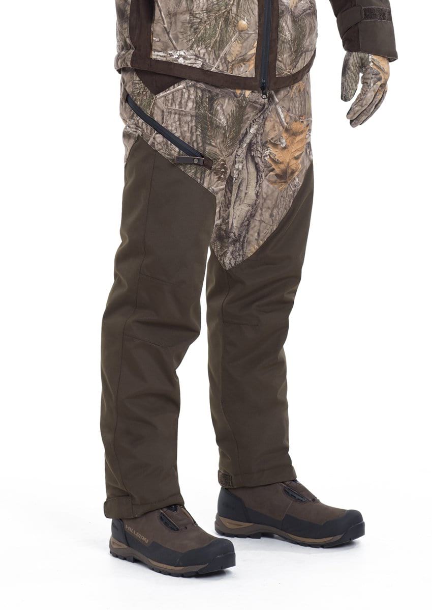 A person wears Hillman® Waterproof Insulated Camo Hunting Pants | Fusion, with only the lower body and one hand visible against a plain white background. Breathable fabric and reinforced legs are featured.