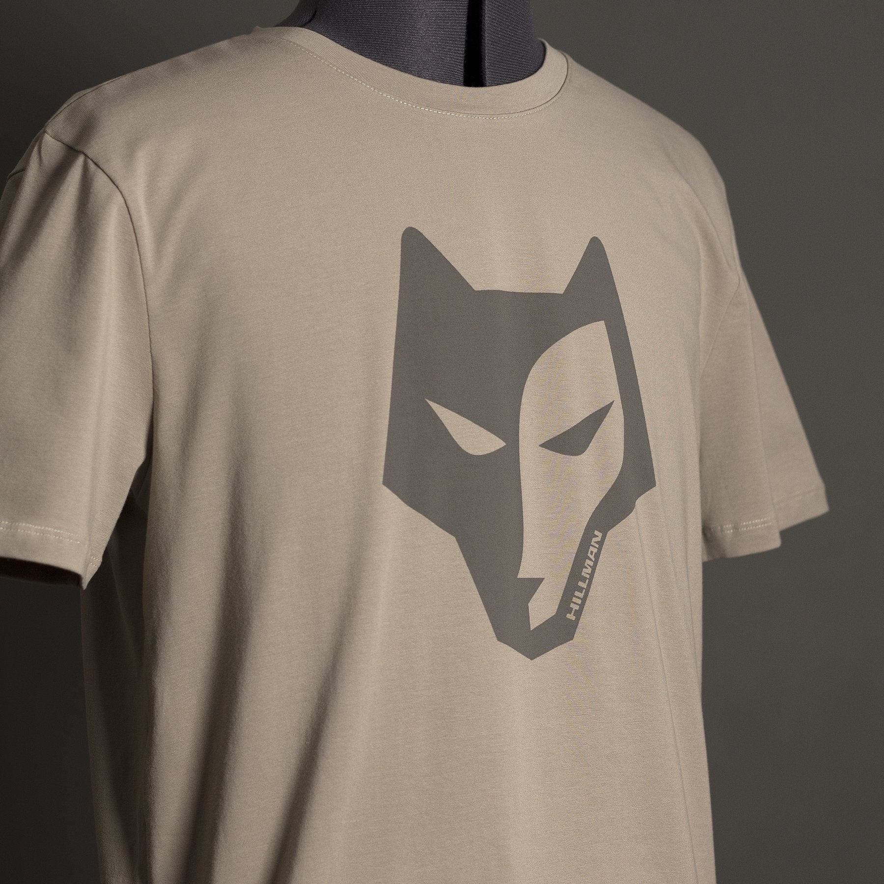 The Hillman® Alpha T-shirt is a beige luxury men’s tee made from Italian Egyptian cotton, featuring a bold dark gray wolf head and “HILLWOLON” text for standout style and comfort.