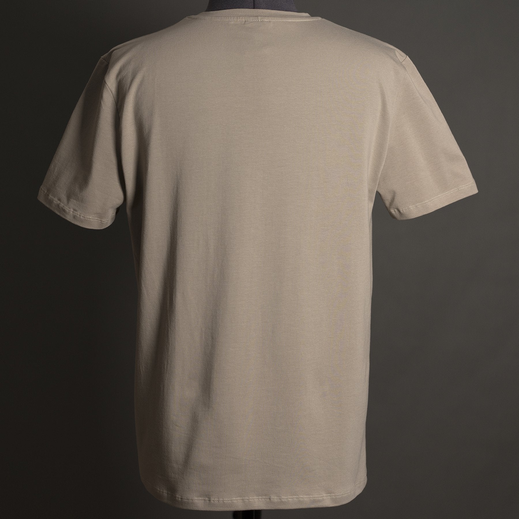 A plain beige Hillman® Alpha T-shirt, shown from the back and made from Italian Egyptian cotton, is displayed on a mannequin against a dark gray background.