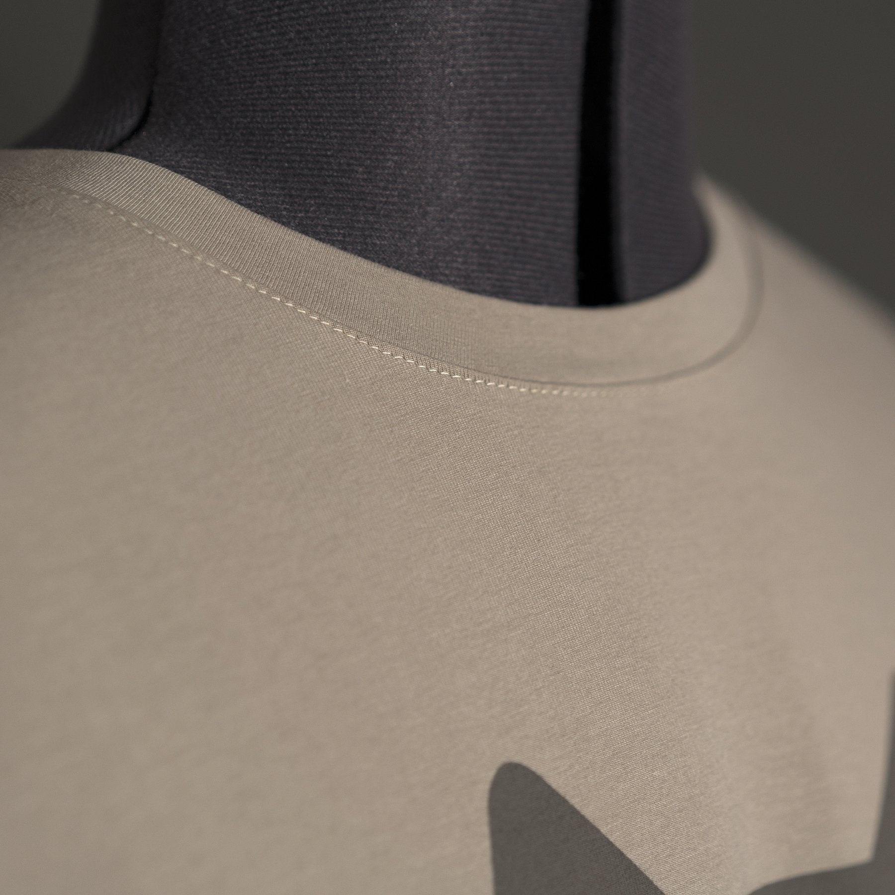 A close-up of a beige Hillman® Alpha T-shirt on a dark mannequin highlights the fine collar stitching, crafted from premium Italian Egyptian cotton.