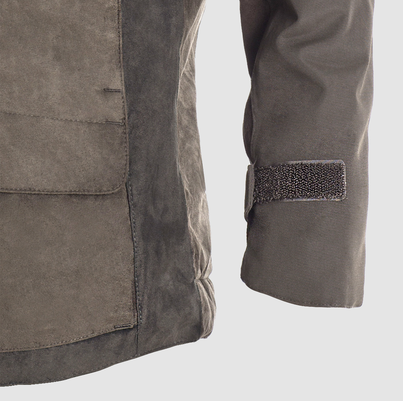 A close-up of the lower left side and sleeve of the Hillman® PRE-ORDER Fusion Hunting Jacket, featuring a large front pocket, seam details, and a Velcro strap on the cuff in durable brown suede.