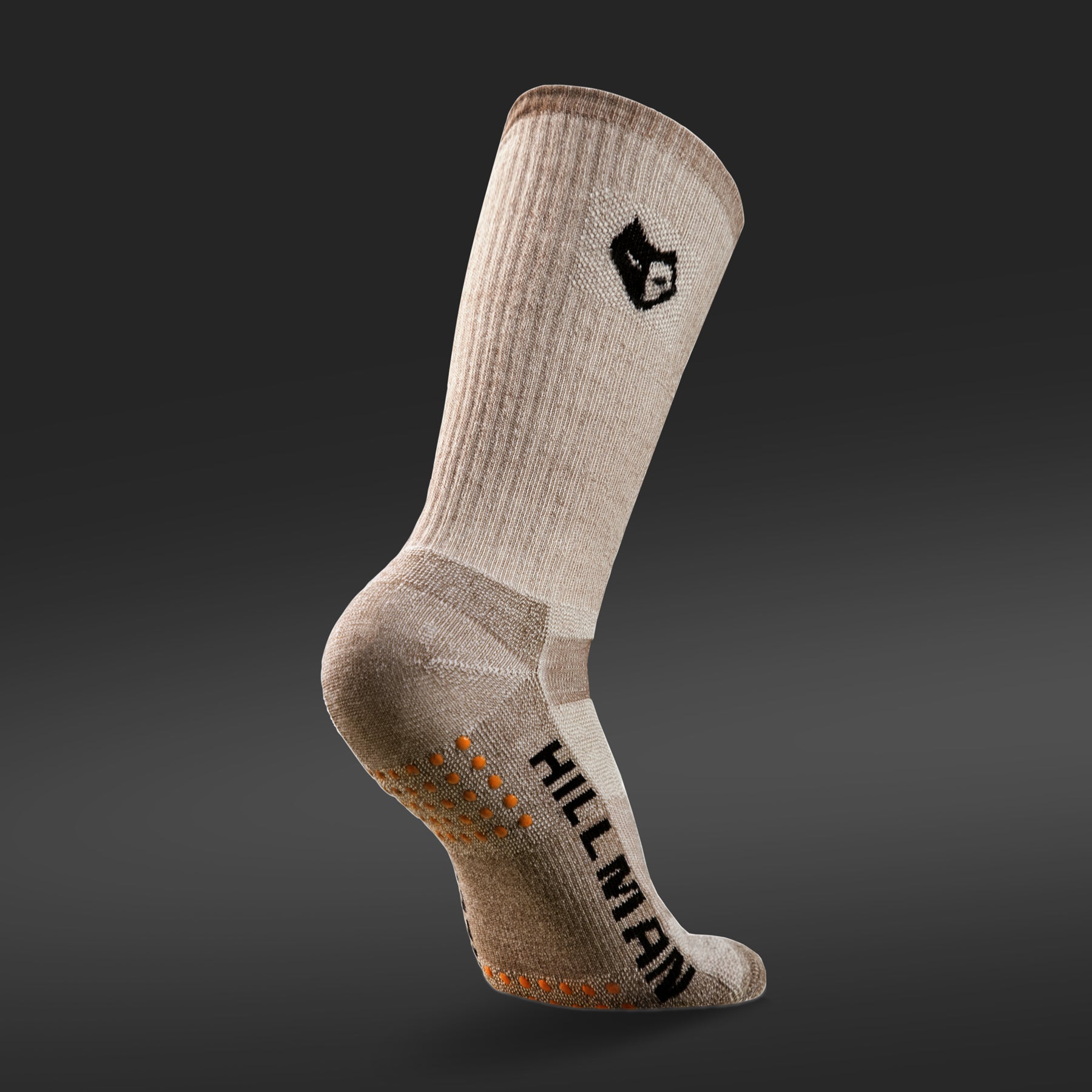 The Ultrawarm merino hunting sock by Hillman®GWR, in beige with a black logo and HILLMAN text, stands out on a dark gradient background. Made from Merino wool with orange grip dots on the sole, it offers thermoregulation for unmatched comfort and style.