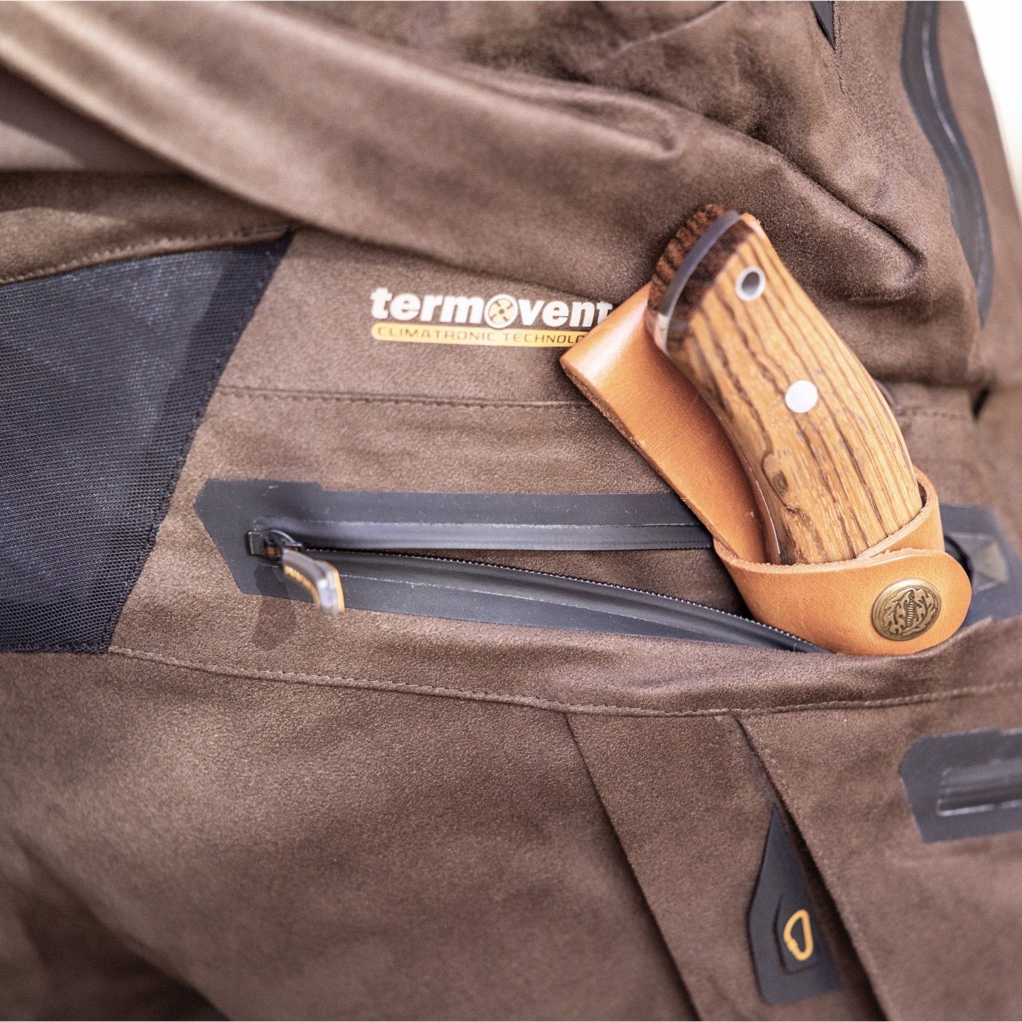 A close-up of a brown pocket with a leather knife sheath and wooden-handled knife, featuring the termovent label—an ideal match for HILLMAN GEAR Insulated Hunting Pants 6OL Cold Weather Waterproof Bibs with Matrix Insulation.