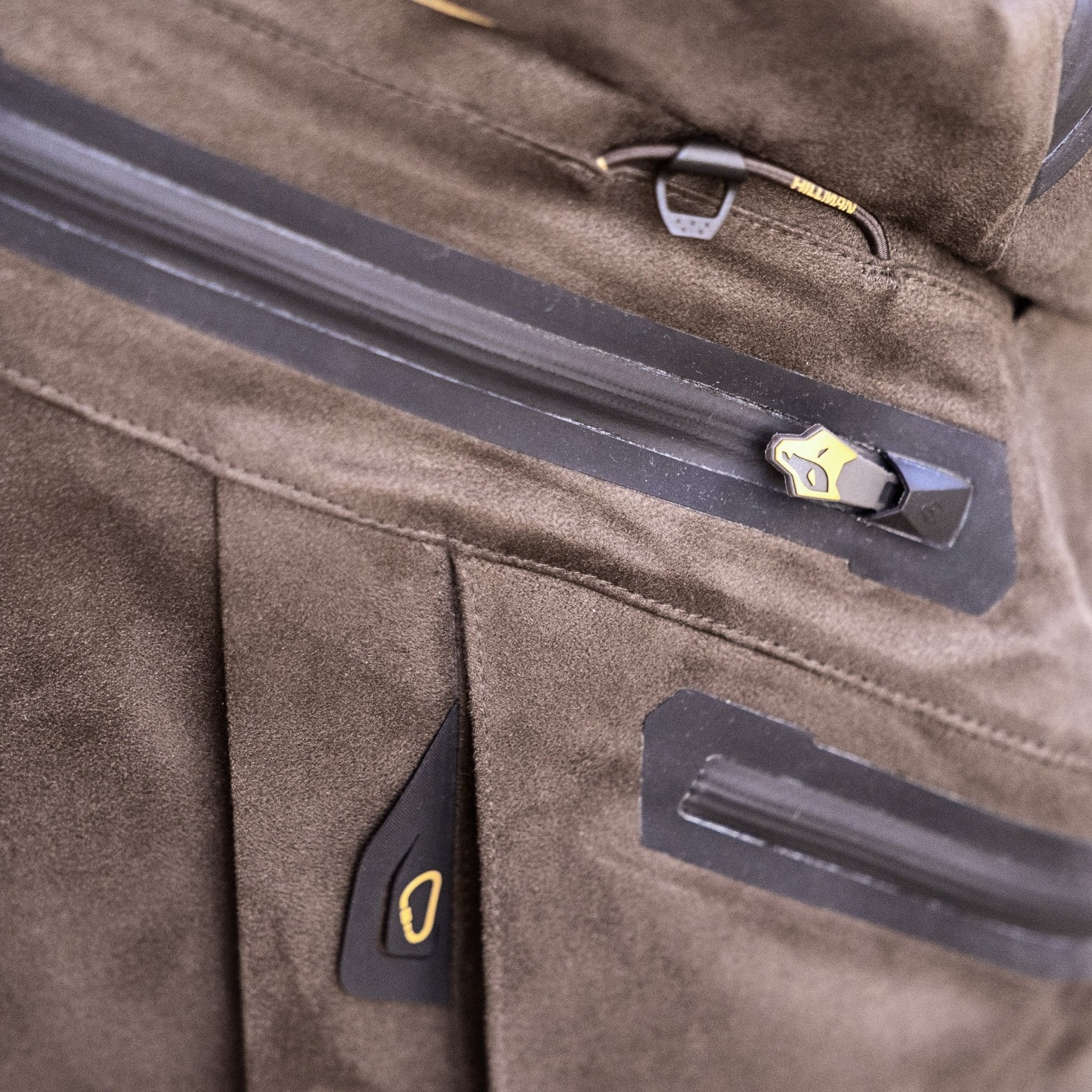 Close-up of a brown suede-like jacket with waterproof zipper, black and gold pull tab, detailed stitching, and black accents—pairs perfectly with HILLMAN GEAR Insulated Hunting Pants 6OL Cold Weather Waterproof Bibs for outdoor adventures.