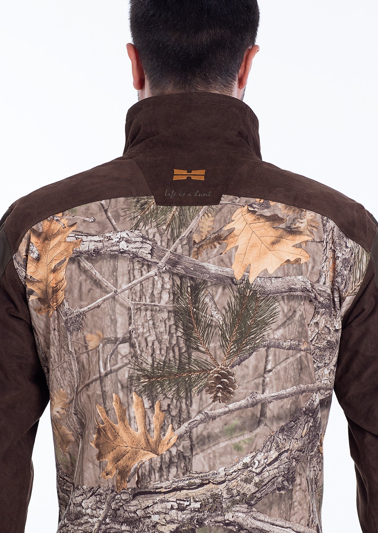 A person is seen from behind wearing the Hillman® Waterproof Insulated Hunting Jacket | Fusion, featuring a brown suede upper and a woodland camouflage lower—perfect for cold weather hunting.