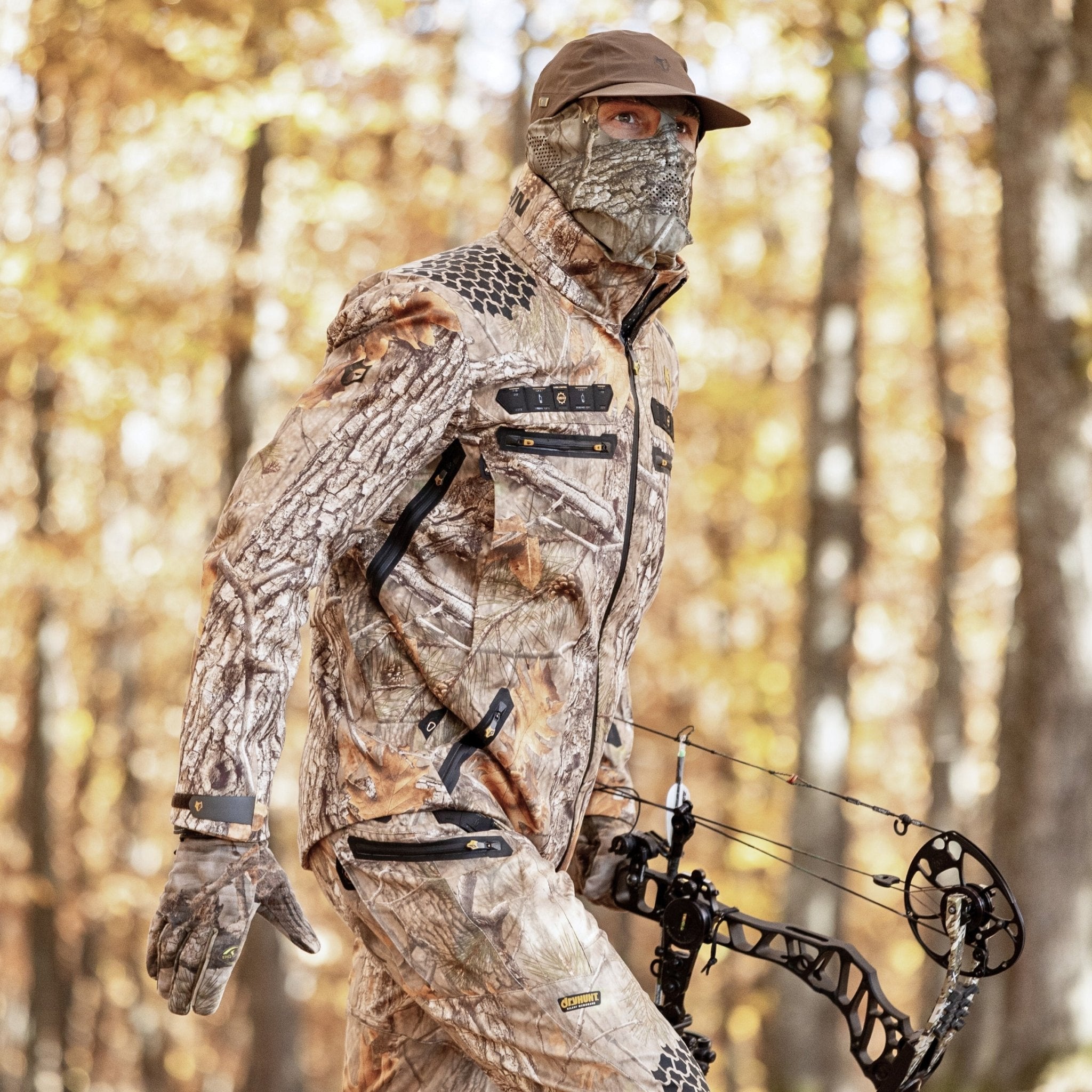 A man with a bow and arrow is prepared for the wild, wearing the Hillman® Camo Hunting Jacket - Insulated Waterproof AlphaShell | 6OL, an essential piece of cold weather hunting gear.