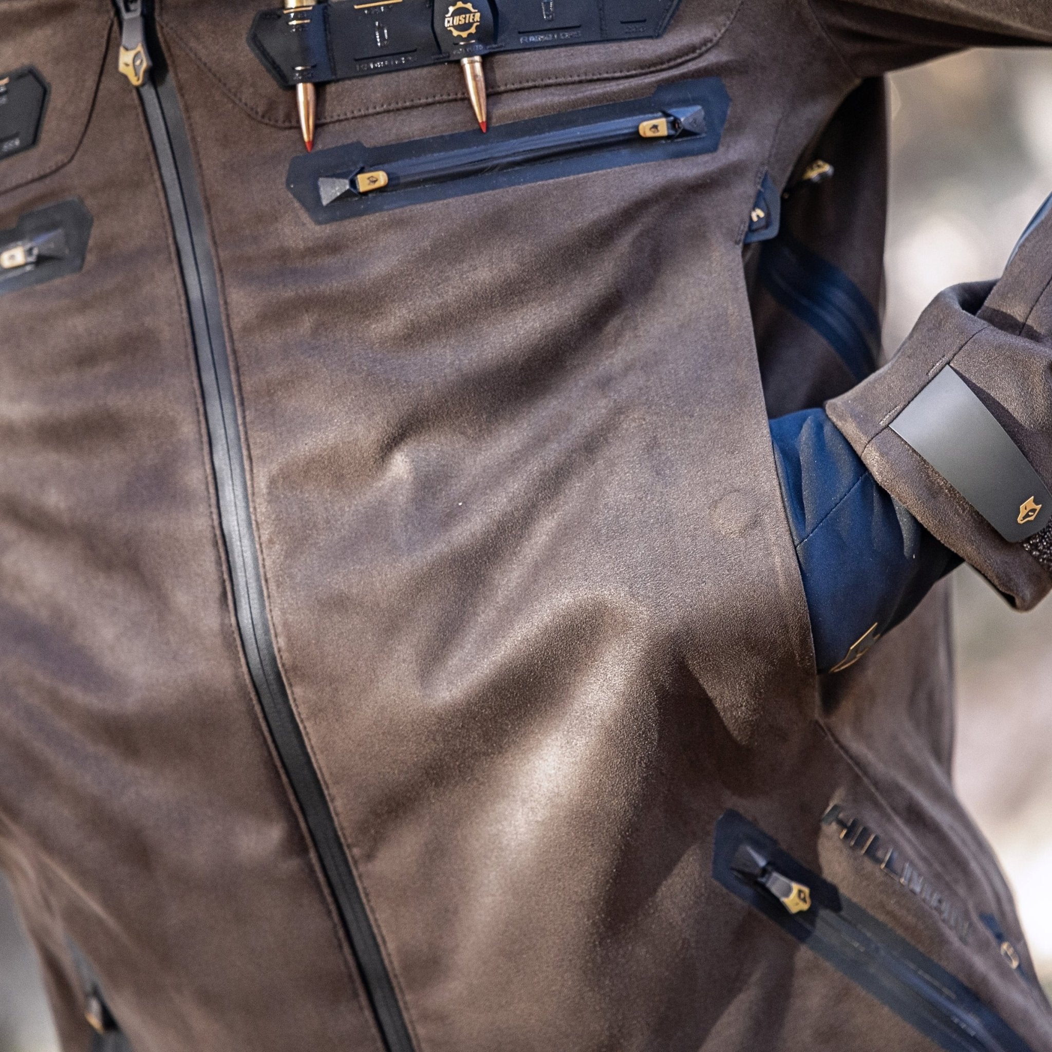 A close-up of the HILLMAN GEAR Camo Hunting Jacket 6OL Heated - Cold Weather Insulated shows a persons arm in a side pocket, highlighting multiple zippers and details, perfect for outdoor adventures.