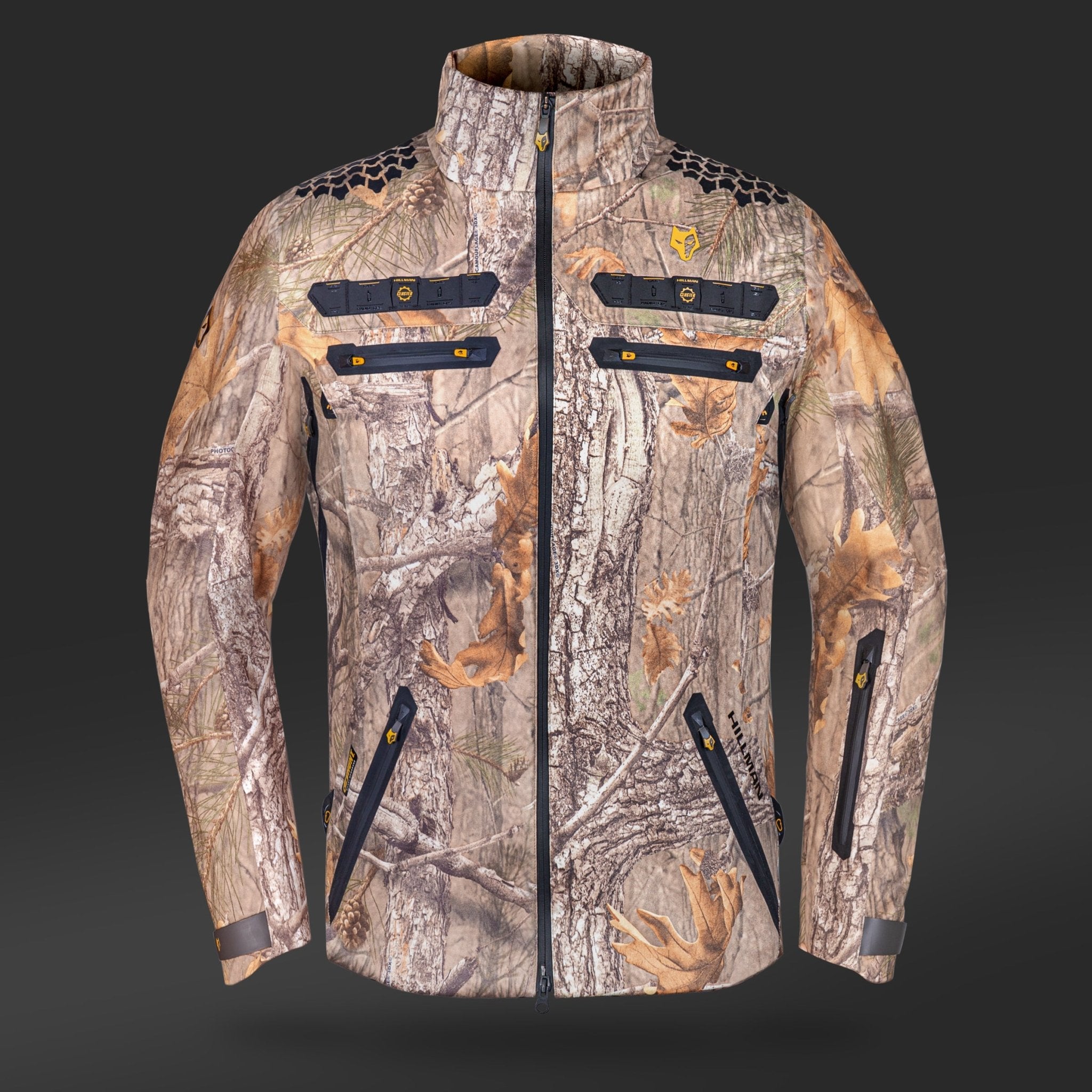 The HILLMAN GEAR Camo Hunting Jacket 6OL Heated features a high collar, black zippers, and multiple zippered chest and side pockets. Designed for cold weather with thermoregulation tech, its displayed against a plain dark background.
