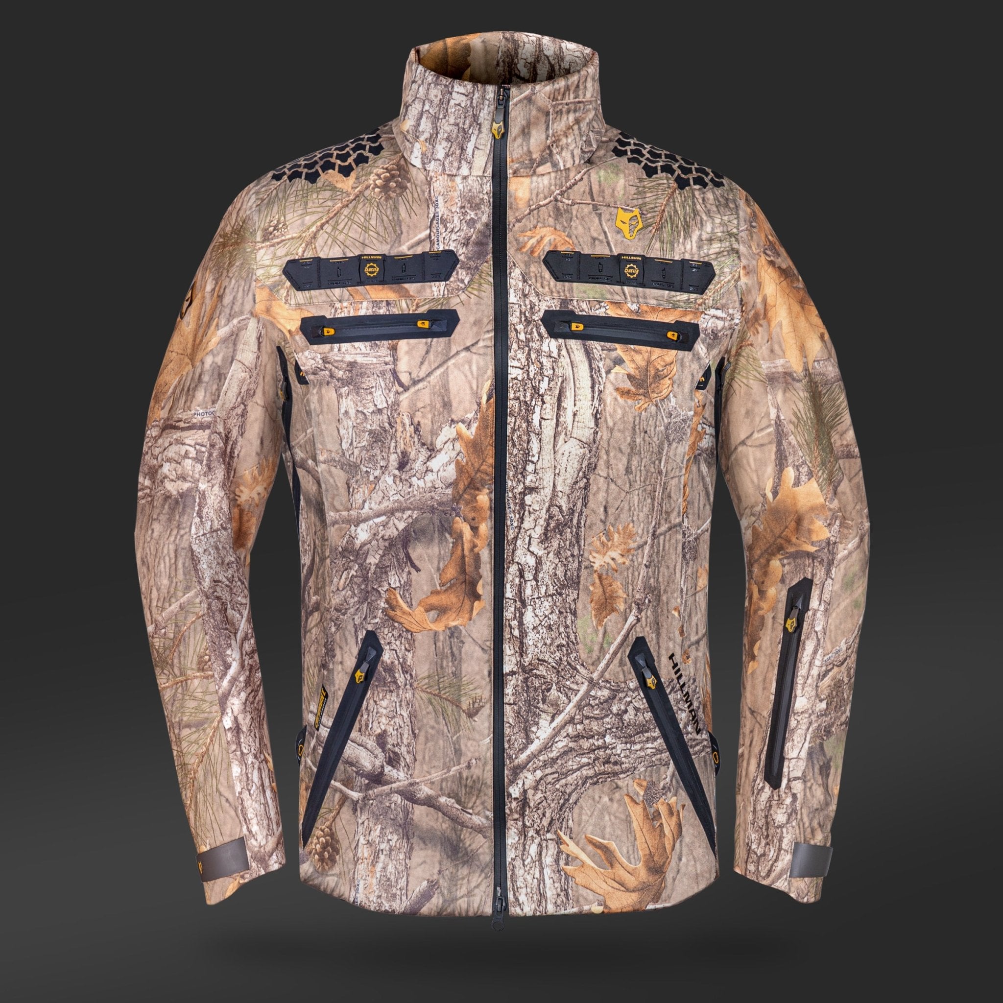 The HILLMAN GEAR 6OL Cold Weather Camo Hunting Jacket features a tree bark and leaf camo pattern on a dark gray background, with a zipper front, multiple black zippered pockets, yellow accents, a high collar, and long sleeves. Perfect for hunting in style and warmth.