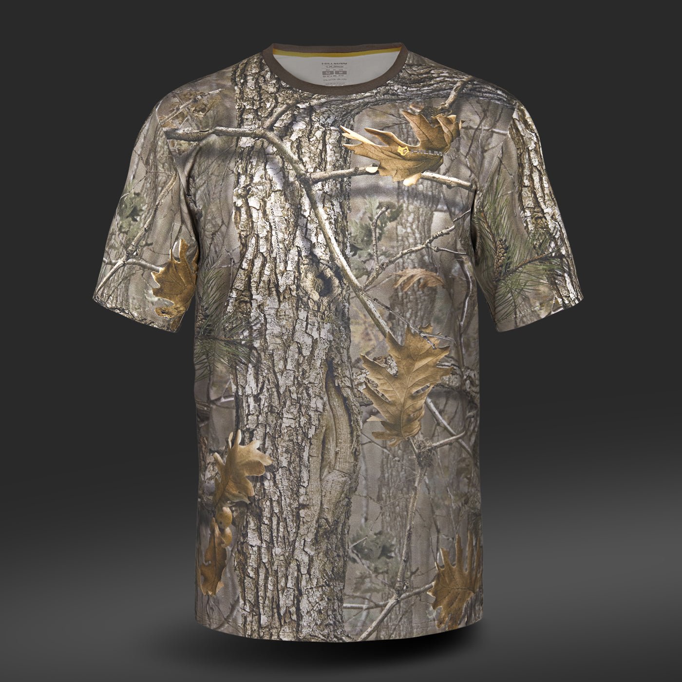 Hillman® Hunting T-shirt DGT Cotton Short Sleeve: A breathable tee with a camouflage pattern of realistic tree bark, branches, and leaves. Made from soft Egyptian cotton, it provides comfort with brown, green, and gray on a dark gray background.